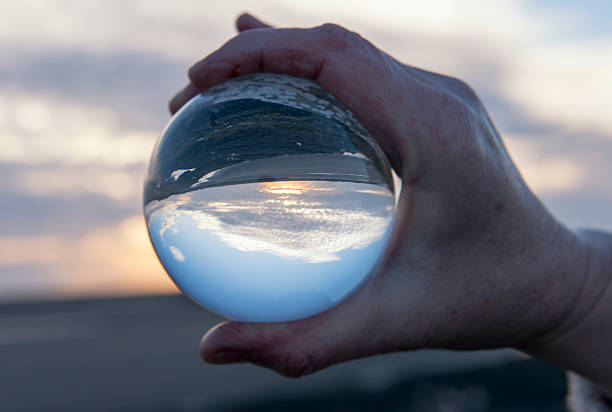 Image of a womans hand holding a glass globe with reflections of a sunset inside it.
